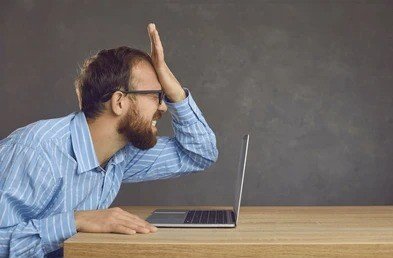 Sorry, a big mistake! A frustrated man in glasses and a striped shirt slaps his forehead while looking at his laptop screen.