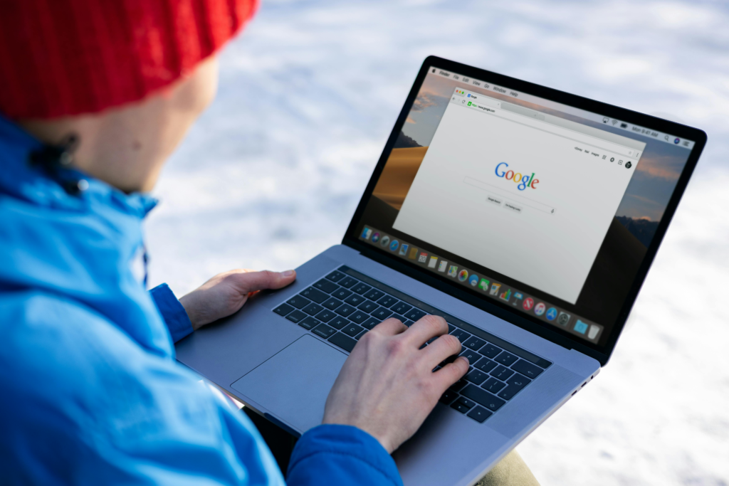 Reputation of a person using a MacBook laptop outdoors in a snowy environment, with the Google homepage open on the screen.
