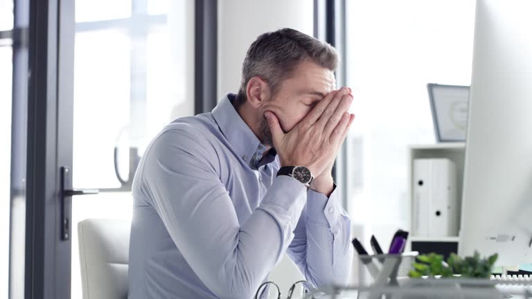 Reputation matters—A stressed businessman in a modern office, covering his face with both hands in frustration.